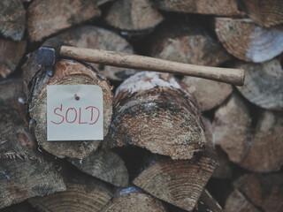 Double-layer firewood forming step with red SOLD tag nailed on, hammer on top, second line of firewood blurred in background, matte soft blue tone, rustic texture, cozy eco-friendly marketing concept.