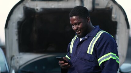 Local African mechanic, small business owner using his smartphone for client video calls, digital banking, and social media in his workshop, SME - Powered by Adobe