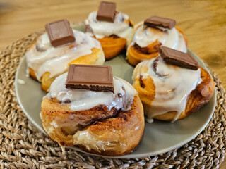 Closeup of freshly baked sweet and delicious cinnamon buns topped with white icing and a square of milk chocolate.