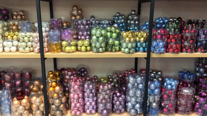 Colorful Christmas ornaments in assorted shades neatly arranged on store shelves, creating a bright and festive holiday display with shiny baubles packed in transparent boxes.
