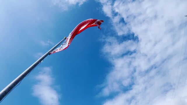 Low-angle shot of the American flag waving against a vivid blue sky and soft clouds—capturing patriotic spirit for Independence Day, Memorial Day, Veterans Day, and Fourth of July themes.