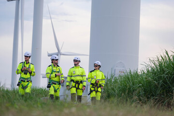 Team of workers in bright suits performing maintenance near wind turbines at a renewable energy site during daylight