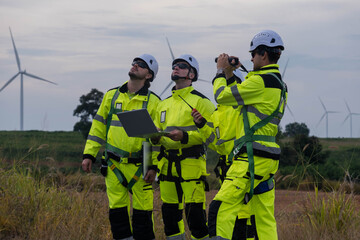 Three technicians assess wind turbines at a renewable energy site while working in bright safety gear during early evening hours