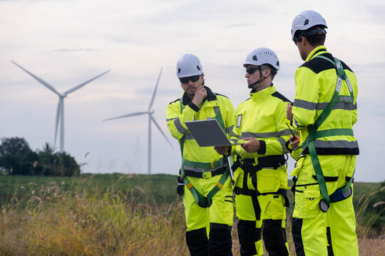 Team discusses project plans while inspecting wind turbines in an open field during late afternoon