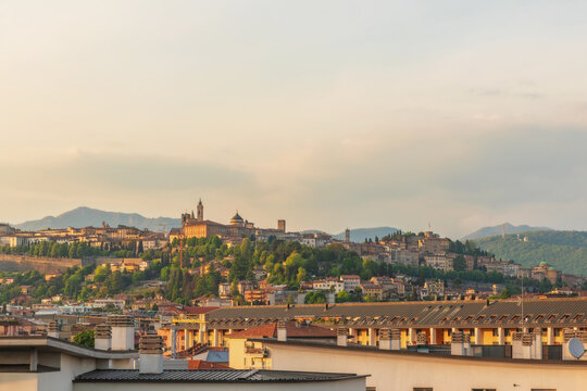 Panoramic view of Bergamo old town at sunset with historical buildings and lush green hills in the background, Lombardy, Italy. Citta alta medieval skyline with its towers, domes