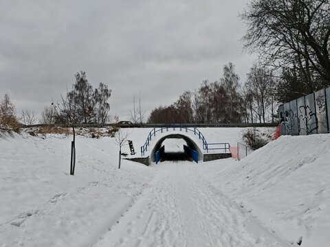 A snow-covered cycling path leads through a tunnel beneath a highway, creating a stark and quiet winter scene along the cold and deserted route - Powered by Adobe