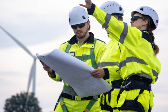 Team of construction workers reviewing plans at a wind farm site during cloudy weather