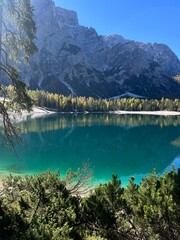 A beautiful view of Lago di Braies, with its crystal-clear turquoise water reflecting the surrounding mountains and trees, creating a peaceful and serene landscape.