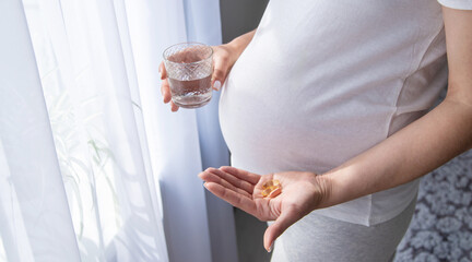 A pregnant woman drinks vitamins and supplements. Selective focus.