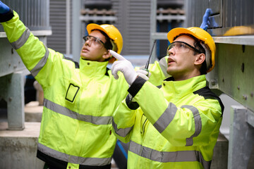 Engineers talk on a walkie talkie and inspecting machinery, wearing hard hats and safety gear in...
