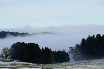 Winterliche Landschaft mit Bergen und W&auml;ldern die von dicken Nebelschwaden durchzogen werden