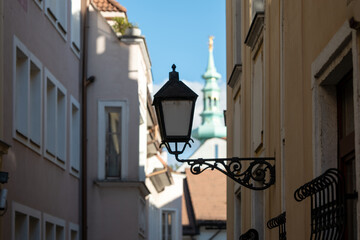 Historic church tower in Bratislava seen between old town buildings, with a vintage street lamp in the foreground.