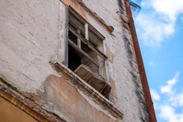 Old damaged building facade with a broken wooden window frame and exposed beams, showing decay and need for renovation.