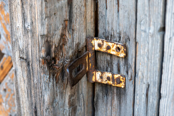 Close-up of a rusty metal latch on old weathered wooden doors, originally used to lock and secure the wooden entrance.