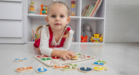 Toddler girl playing with a wooden educational puzzle and sorting shapes on the floor at home.