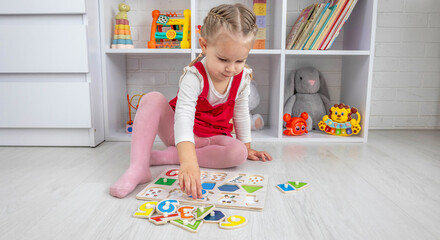 Fototapeta premium Toddler girl playing with a wooden educational puzzle and sorting shapes on the floor at home.