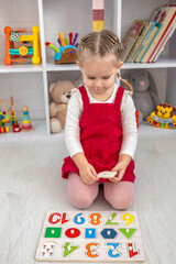 Toddler girl playing with a wooden educational puzzle and sorting shapes on the floor at home.