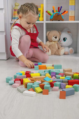 Little girl building a tower with colorful wooden blocks on the floor.