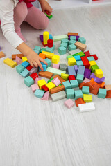 Little girl building a tower with colorful wooden blocks on the floor.