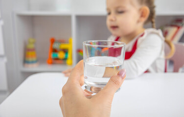 Mother's hand giving a glass of clean drinking water to a young child sitting at a table