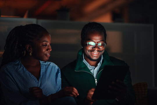 Young colleagues happily interacting with digital tablet at night
