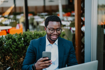 Young black businessman using phone outdoors cafe