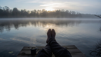 First-Person View of Person Relaxing on a Wooden Dock with Feet Up and Coffee Mug by a Misty Lake