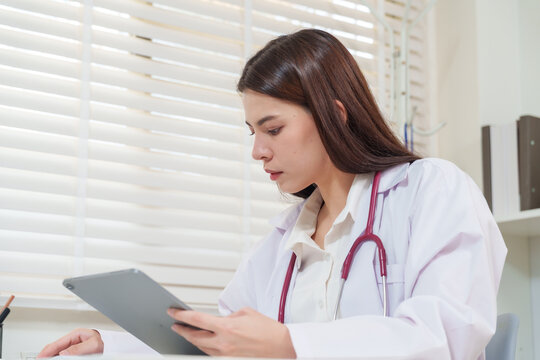 Asian female doctor wearing stethoscope using tablet to review medical record for telemedicine consultation giving online prescription advice and healthcare diagnosis through telehealth platform - Powered by Adobe