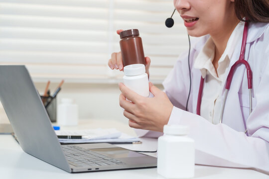 Asian female doctor showing two medicine bottles during telemedicine consultation providing healthcare advice and prescription explanation to patient via online digital telehealth communication
