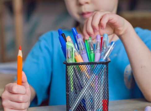 Child's Hands Selecting a Pencil from a Cup of Colorful Art Supplies - holding a single orange pencil
