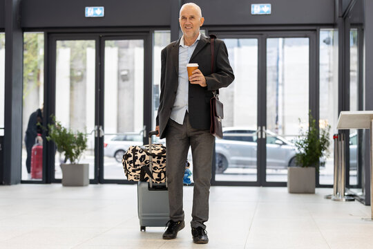 Mature man traveling carrying luggage and coffee at airport