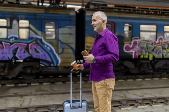Male traveler waiting on train platform with smartphone and coffee - Powered by Adobe
