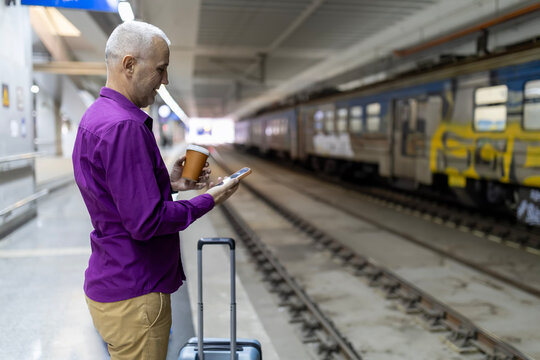 Man waiting for train using smartphone drinking coffee