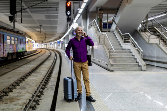 Smiling senior man traveling talking on smartphone standing at train station