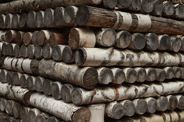 The corner of a wooden woodpile made of birch firewood with rounded ends closeup