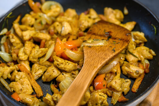 Close-up of sautéed turkey pieces with onion and bell pepper in a pan, stirred with a wooden spatula during cooking.
