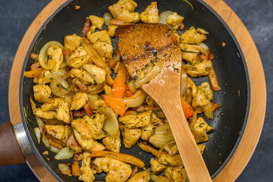 Freshly fried turkey chunks mixed with onion and pepper slices in a skillet, with a wooden spatula resting on top. - Powered by Adobe