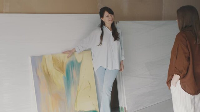 Woman discussing colorful art piece in studio with friend while exploring creative expression in painting