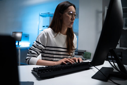 Asian woman wearing reflective glasses typing code on a keyboard. Freelance programmer working overtime in the office. Software development, cybersecurity, program developer. - Powered by Adobe