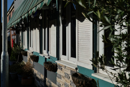 Building exterior featuring closed white shuttered windows under a green awning. The stone facade and potted plants add to the storefront's charm in Heywood - Greater Manchester - UK