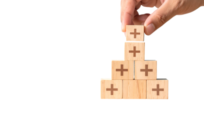 Hand placing wooden block with plus sign atop a pyramid, with black negative space