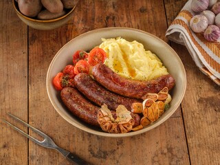 Juicy pork sausages sit alongside velvety mashed potatoes and ripe tomatoes, crafted for a comforting meal that captures the essence of rustic Romanian cooking