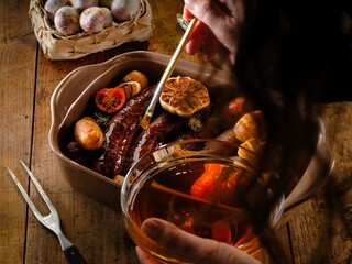 Enjoy a delicious plate of traditional Romanian cuisine featuring roasted pork sausages, golden potato wedges, garlic cloves, and fresh herbs. Perfect for a hearty meal