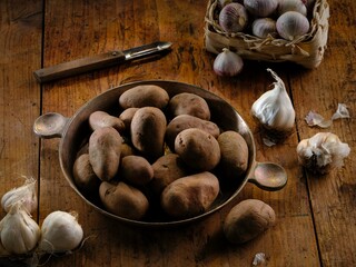 Freshly harvested potatoes sit in a rustic metal bowl alongside whole garlic cloves, preparing for a hearty Romanian dish that warms the soul during winter nights