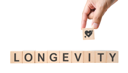 Hand placing heart symbol block above "LONGEVITY" spelling wooden blocks