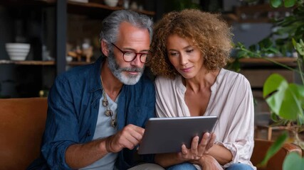 Mid adults couple planning their future together using a tablet while relaxing indoors in a cozy setting