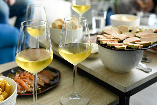 Sc&egrave;ne d'ap&eacute;ritif compos&eacute; de plusieurs verres de vin blanc et d'assiettes de foie gras et saumon fum&eacute;, sur des tables basses dans un salon de jour