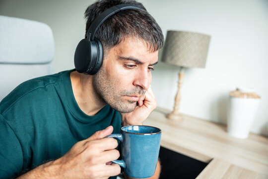 Thoughtful Latin man wearing headphones working from home
