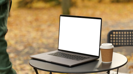 Laptop and coffee cup on a table outdoors with autumn foliage in the background