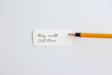 Reminder Note to Buy Milk and Call Mom with Yellow Pencil on White Background Ready to Fulfill Daily Tasks and Responsibilities at Work
